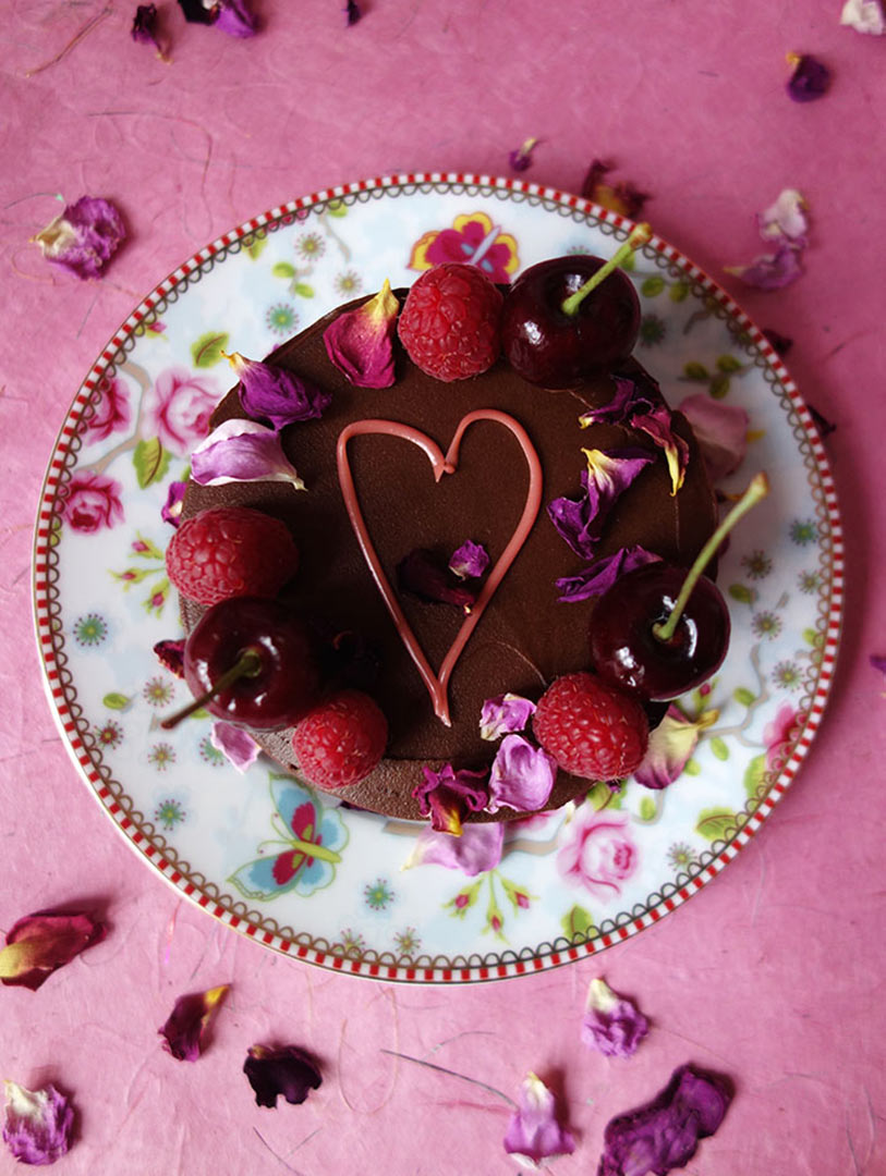 Award-winning gluten free rich mini chocolate cake made with organic ground almonds and dark chocolate, and Jamaica Rum. Covered with dark chocolate ganache and decorated with piped pink heart in organic white chocolate, cherries, berries & edible rose petals. All ingredients glutenfree. Available diary free