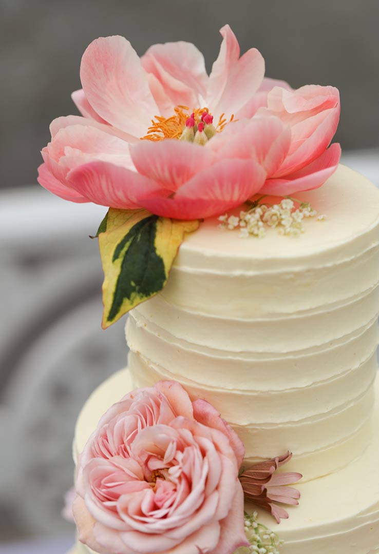 A layered Tunisian Orange & Almond Cake, for a wedding. Three tiers, made with gluten free ingredients: organic ground almonds, oranges and extra-virgin olive oil. Filled and frosted with Swiss meringue buttercream and decorated with organic edible peonies and roses. All ingredients gluten-free. Photo by Minna Rossi