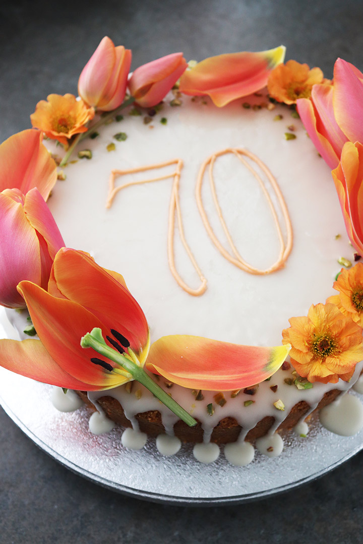 Lemon and Pistachio Cake, made with gluten free, wheat free ingredients. Topped with a lemon glaze and decorated with piped message, seasonal flowers and nibbed pistachios. All ingredients gluten-free, wheat-free