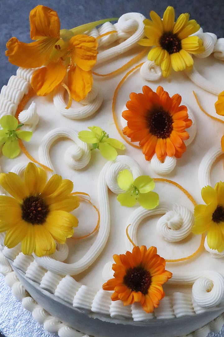 For a gluten free first wedding anniversary – a small glutenfree orange and almond cake, filled and frosted with lemon buttercream. All ingredients gluten-free. Decorated with piped buttercream, orange zest and organic edible alloment flowers